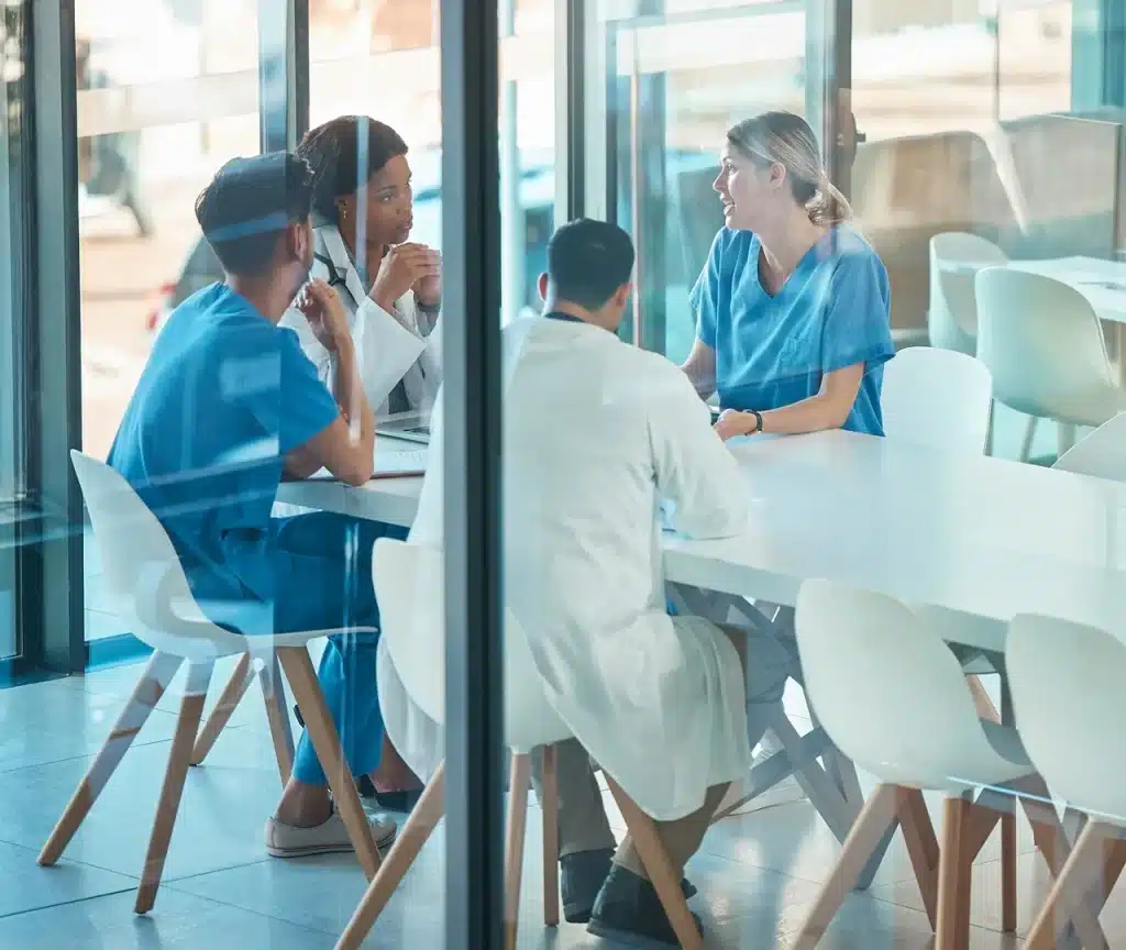 Group of healthcare professionals in scrubs and lab coats meeting around a conference table in a modern medical facility